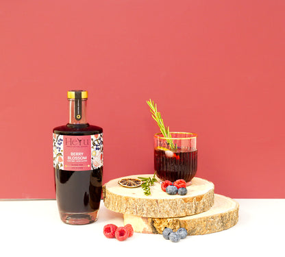 Bottle of HeYu Berry Blossom mocktail with a glass of cocktail on a wooden stand against a red background