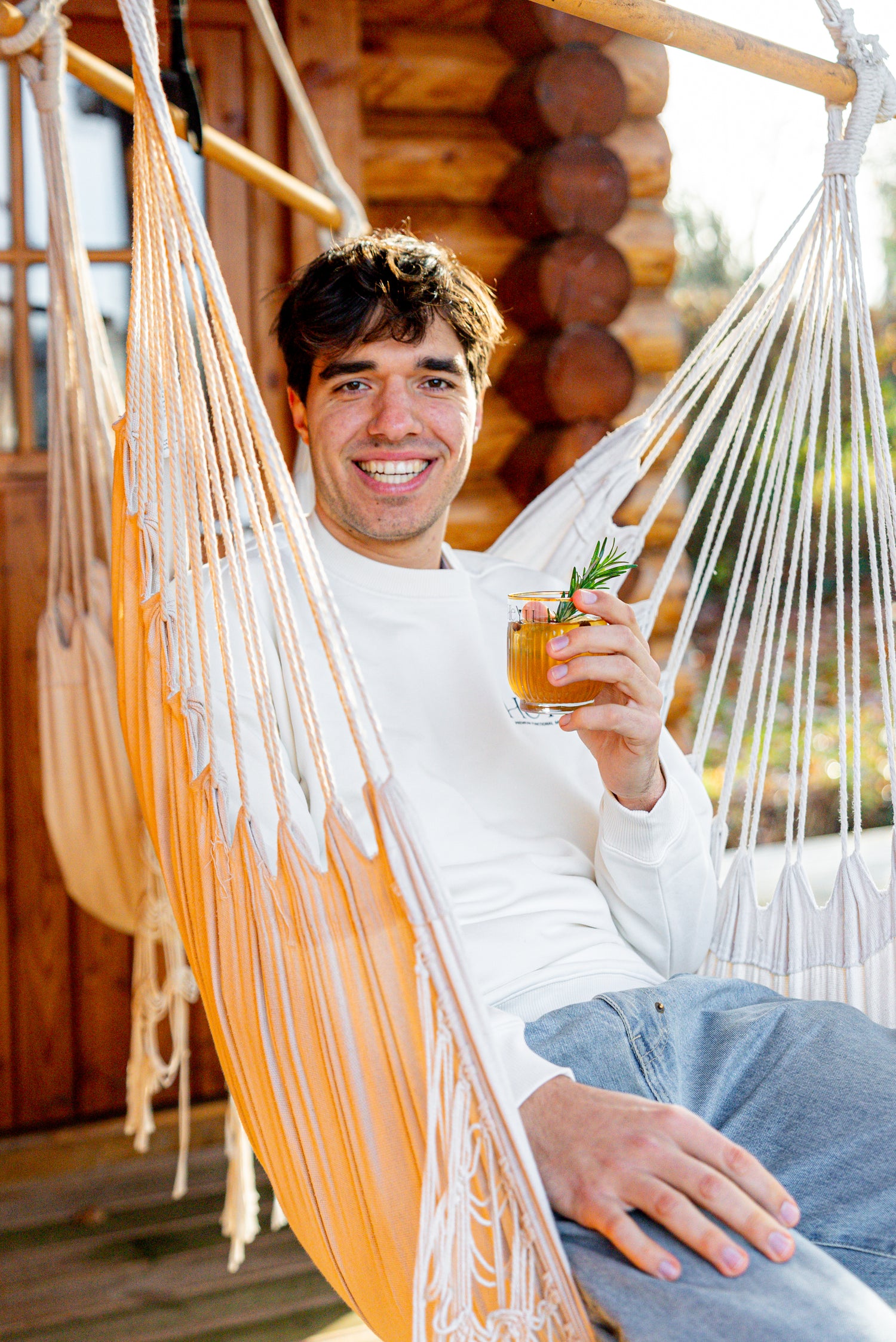 A man sitting on a hammock with a glass of Heyu Spicy Peach Vanilla