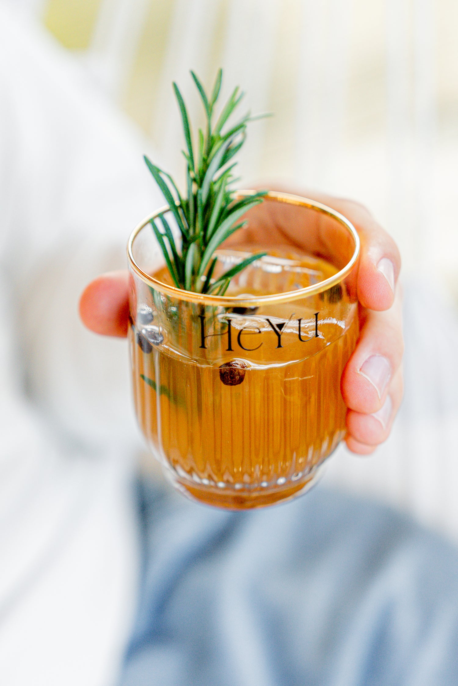 Picture of a hand holding a Heyu Spicy Peach Vanilla mocktail with a sprig of rosemary