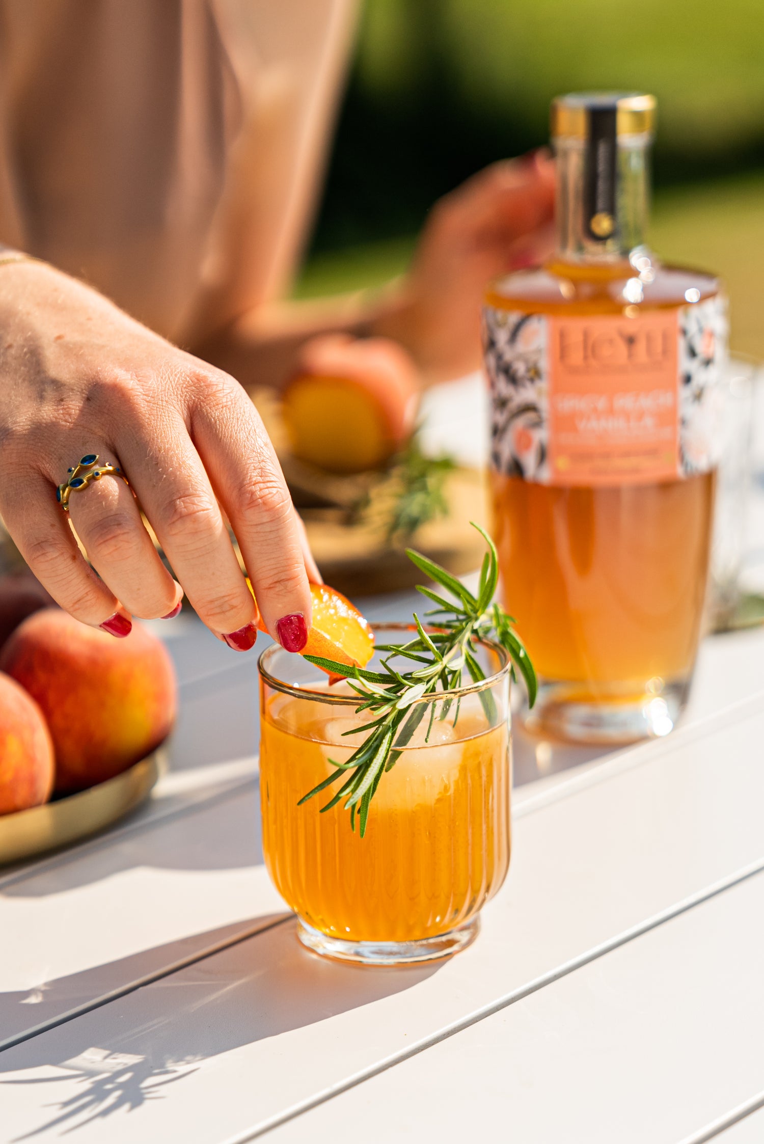 A women putting a slice of peace in a glass of Heyu Spicy Peach Vanilla Mocktail